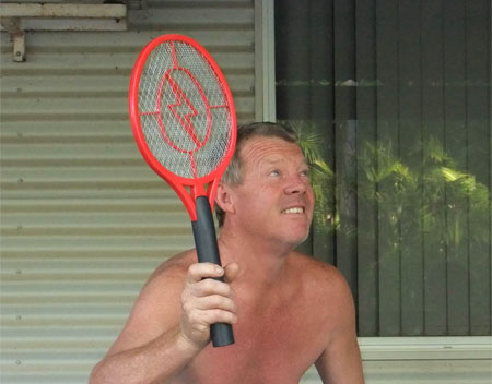 photo of a shirtless middleaged sunburned white man with a raquet bug zapper